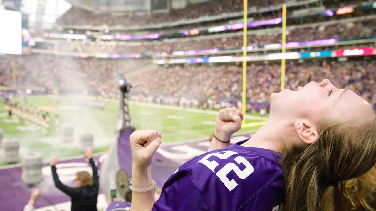 Woman in Vikings jersey cheering from her seat in the packed stadium